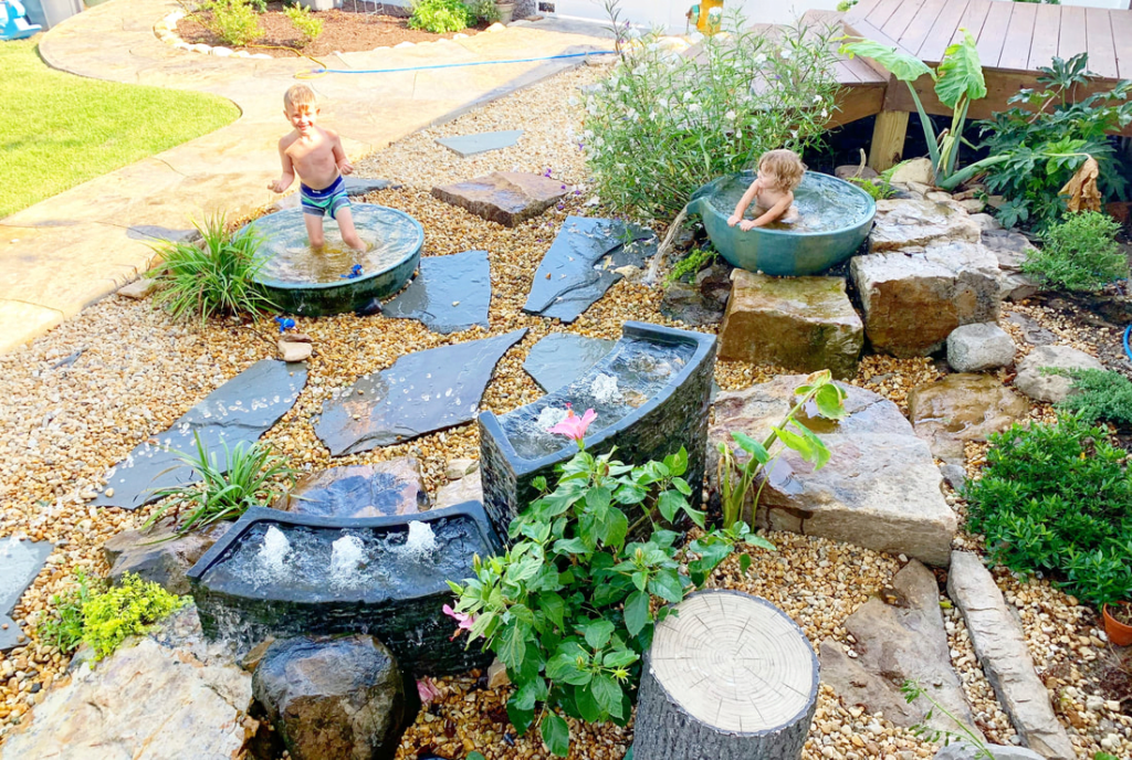 Children playing at interactive bowl fountains beside flagstone stepping stones.
