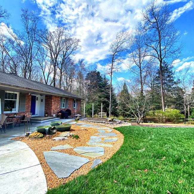 Flagstone path through a gravel bed with boulders in front of a brick ranch home.