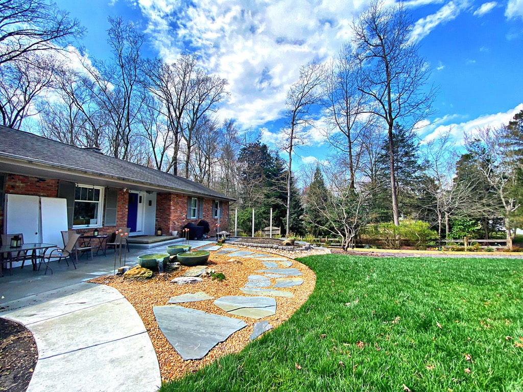 Flagstone path through a gravel bed with boulders in front of a brick ranch home.