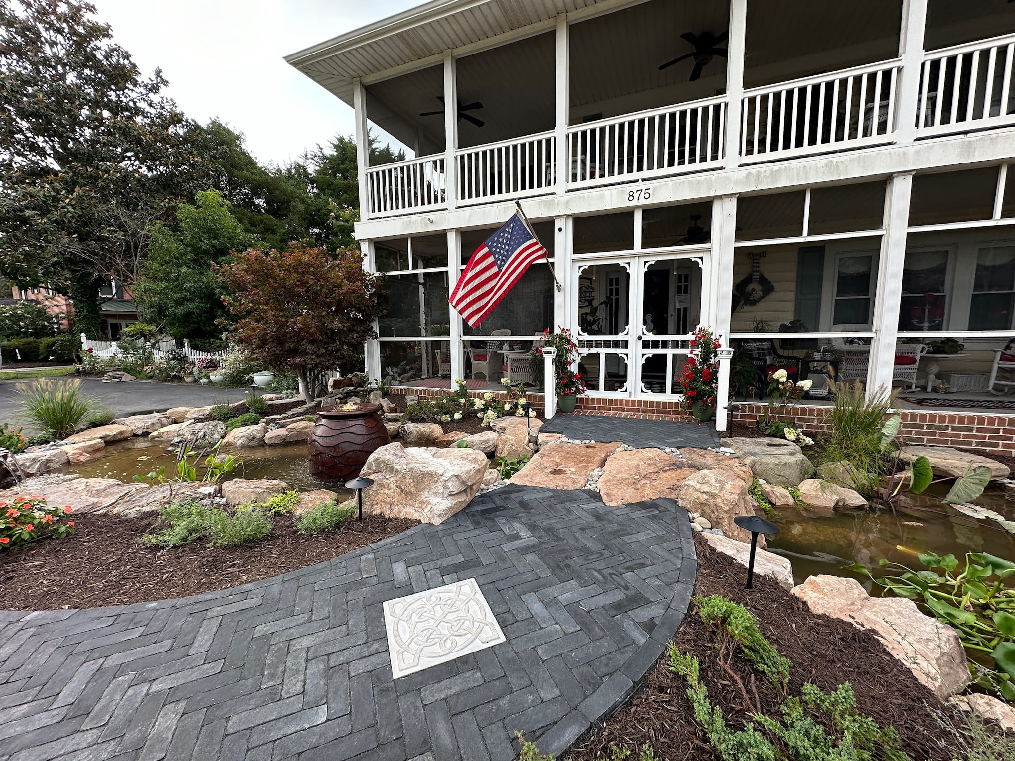 Front yard koi pond and waterfall with boulders below a white two-story porch.