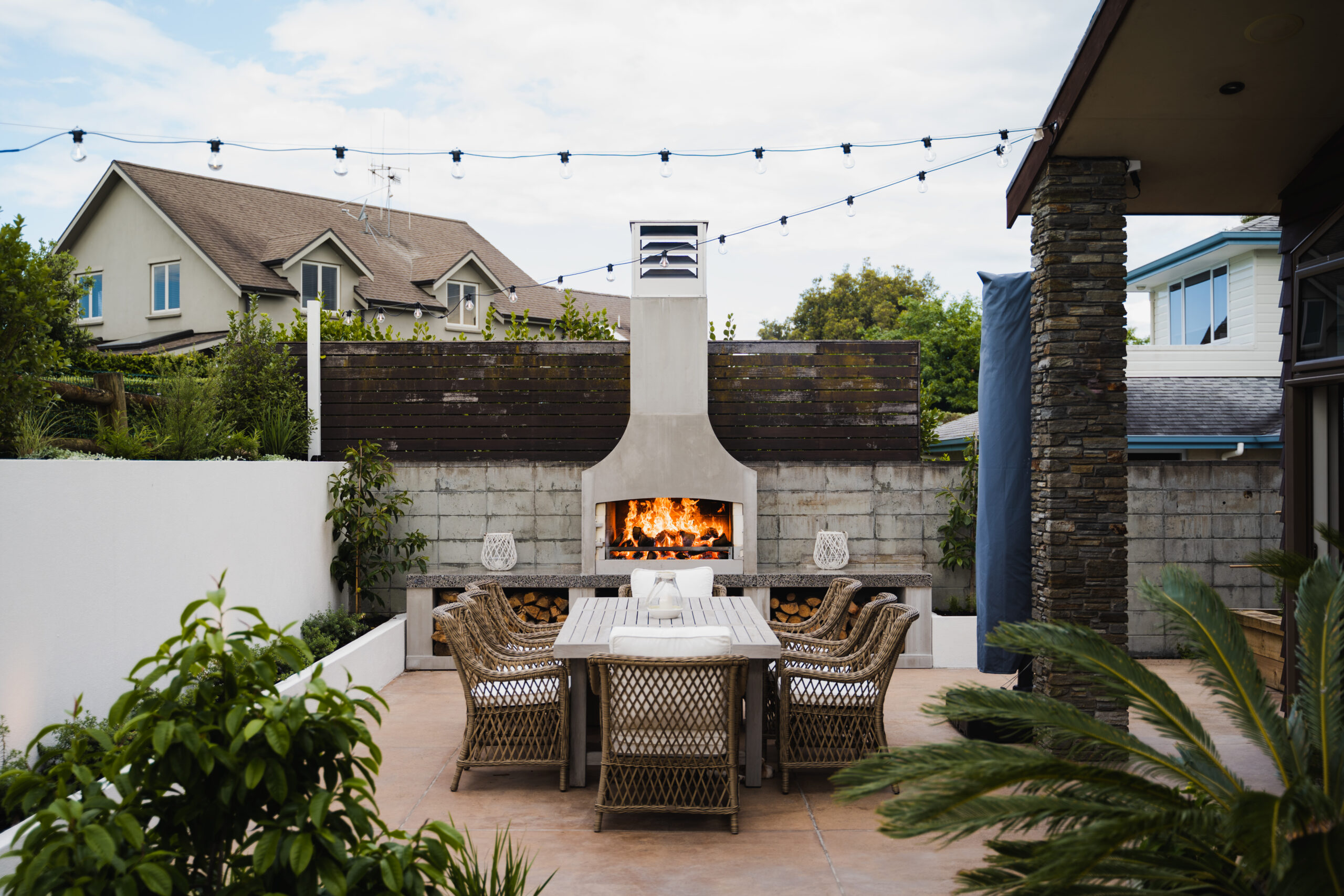 Outdoor fireplace and dining area under string lights on a walled patio