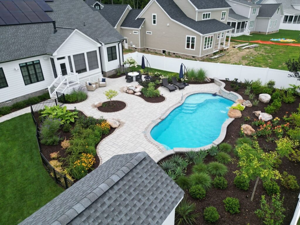 Aerial view of a freeform pool with paver deck and landscaped beds in Tabb, VA
