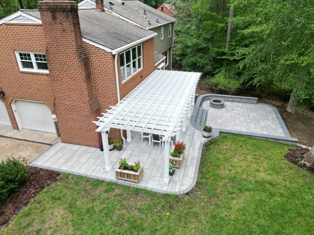 Aerial view of a white pergola and paver patio beside a brick home