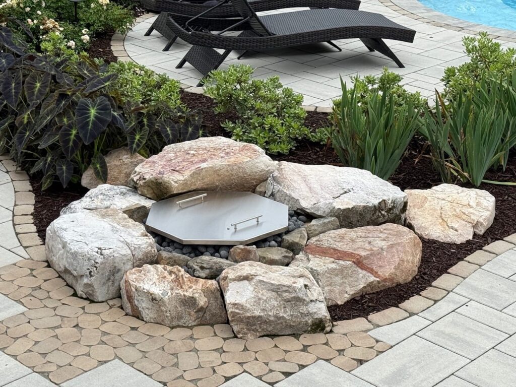 Boulder-ringed fire pit with metal cover on a paver patio in Tabb, VA