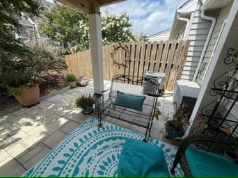 Covered patio with teal rug and bench beside the home