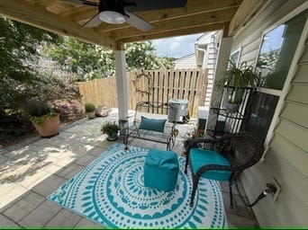 Covered patio with teal rug, chairs and ceiling fan