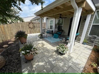 Covered paver patio with potted flowers and teal seating