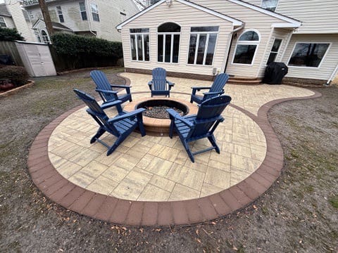 Curved tan paver fire pit patio with red border and blue Adirondack chairs