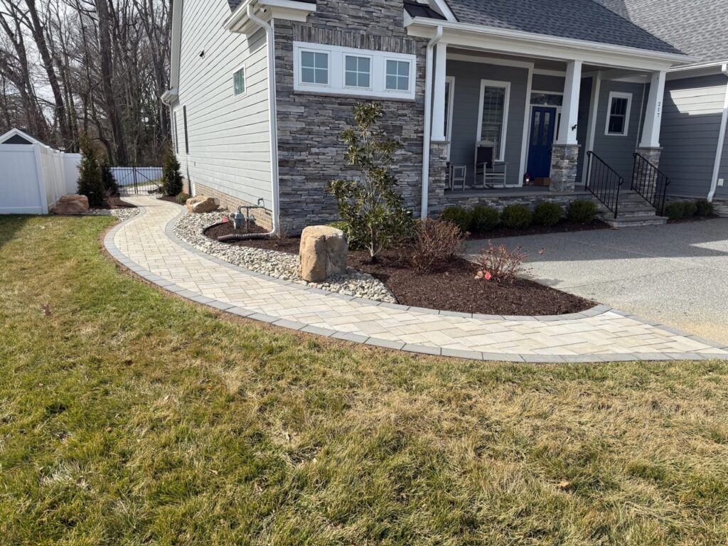 Curved paver walkway with mulch beds and boulder in a front yard