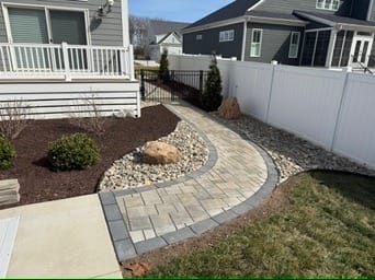 Curved paver walkway with dark border along a white vinyl fence
