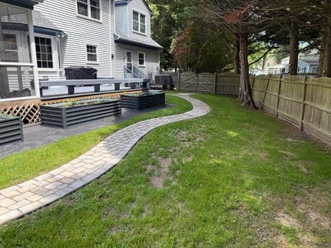 Curving paver path beside a patio with raised beds and screened porch