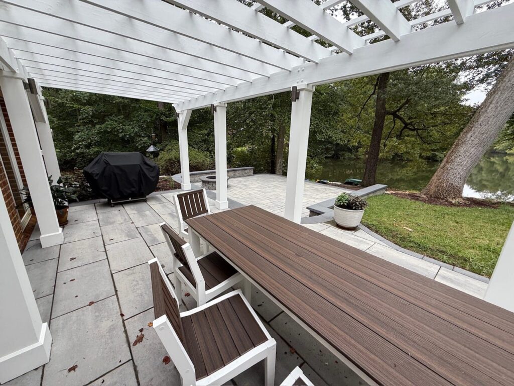 Long dining table under a white pergola on a paver patio