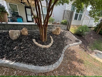 Edged mulch bed with crape myrtle and boulders beside a patio wall