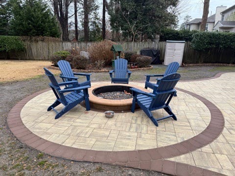Fire pit with blue Adirondack chairs on a round paver patio