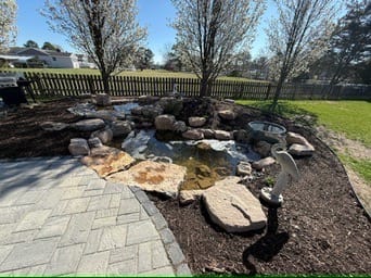 Herringbone paver patio edge meeting a boulder pond