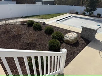 Mulch planting bed with shrubs and boulder beside a pool deck