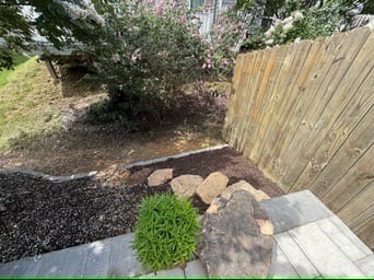 Mulch bed with stepping stones and shrub along a wood fence