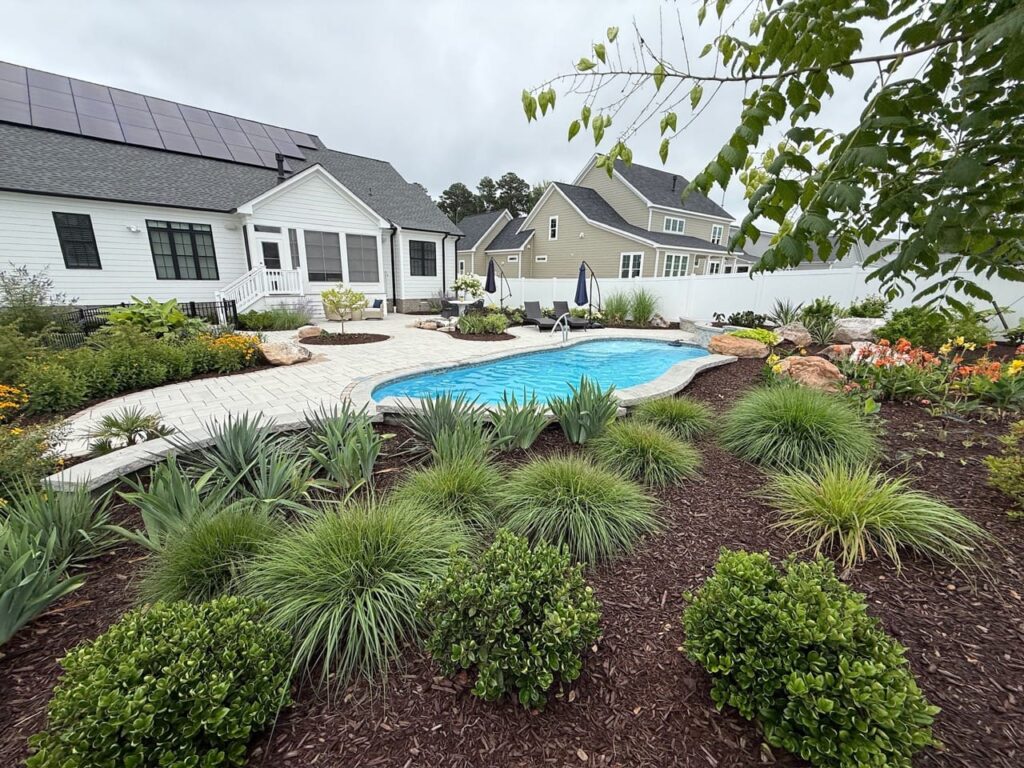Ornamental grasses and shrubs in a mulch bed beside a pool in Tabb, VA