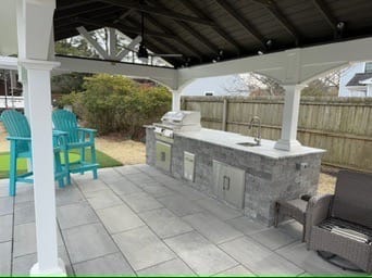 Stone-veneer outdoor kitchen with grill under a pavilion in Poquoson, VA