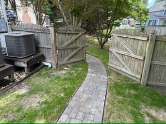 Paver path leading through an open wood fence gate