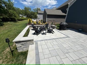 Paver patio with dining set and stone seat wall beside a home
