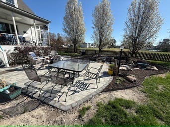 Paver patio with dining table and chairs beside new planting beds
