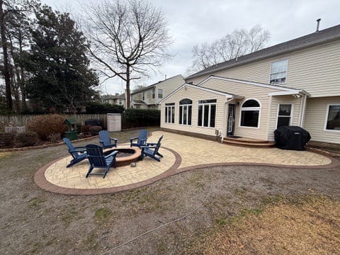Wide view of a paver patio and fire pit circle behind a home