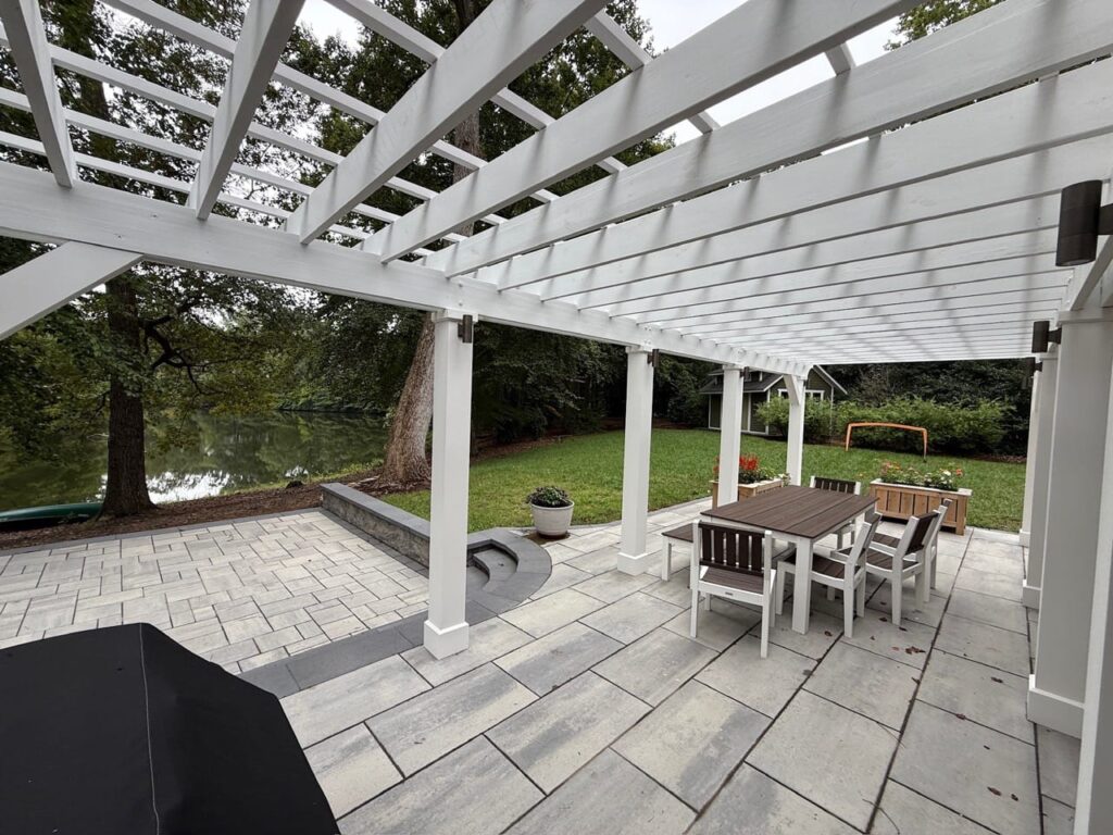 Paver patio under a white pergola with dining set and grill