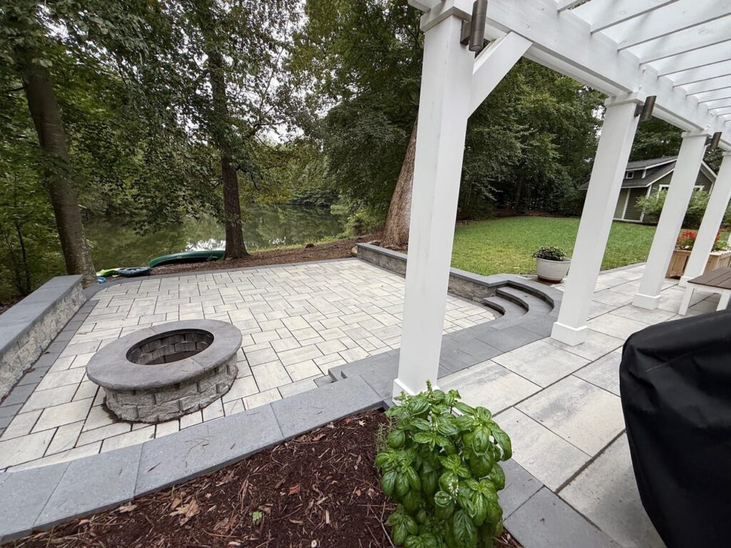 Round fire pit on a sunken paver patio beside a pergola