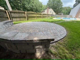 Round raised paver patio with retaining wall edge in a fenced yard