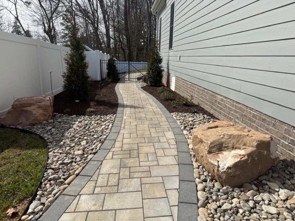 Side-yard paver walkway with river rock borders and boulders
