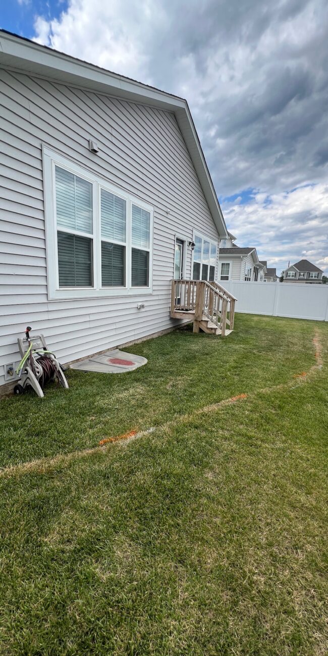 Before photo of a side yard lawn with a painted layout line next to a gray house in Glen Allen, VA.