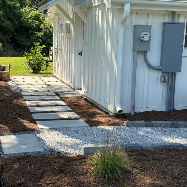 Paver stepping stones set in white gravel lead past mulch beds beside a white cottage in White Stone, VA.